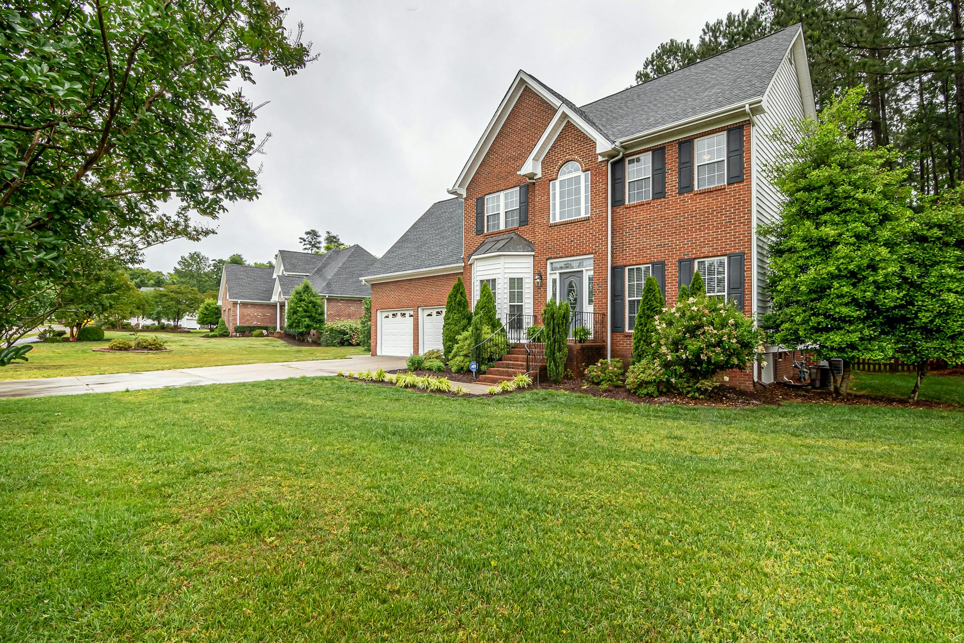 Charming two-story brick house with manicured lawn and trees, perfect family home.