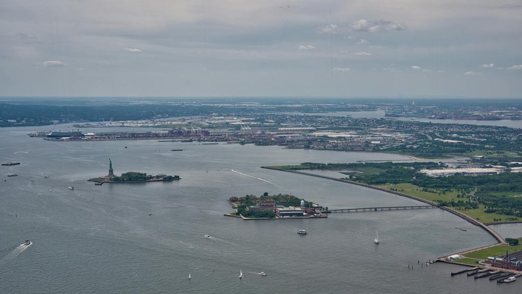 Aerial view of the iconic Statue of Liberty and expansive New York Harbor on a clear day.