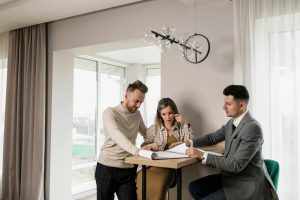 A couple consults with a real estate agent in a modern indoor setting, reviewing property documents.
