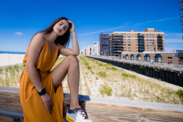 Fashion model in yellow dress sitting by urban beachfront on a sunny day.