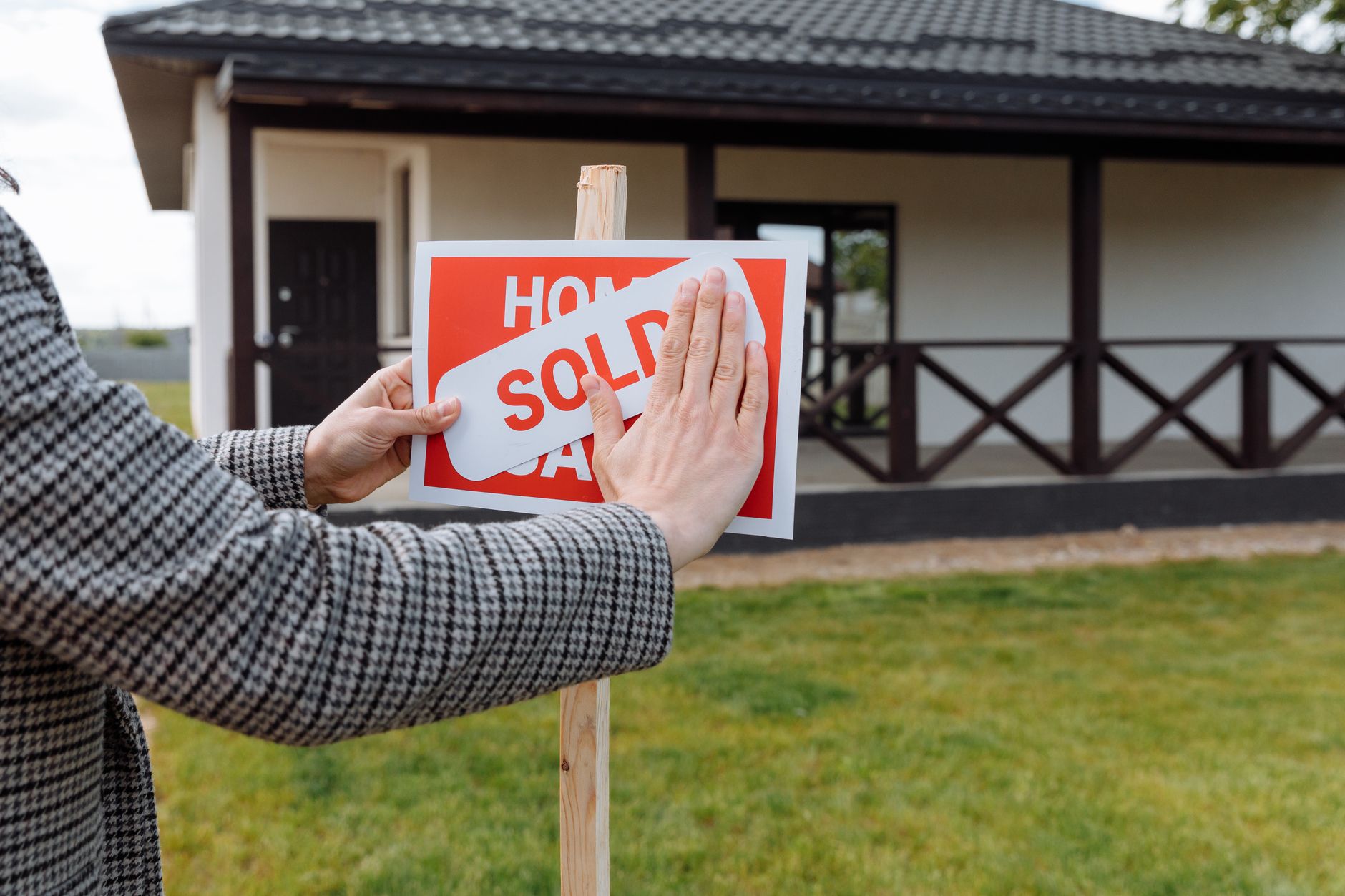 Close-up of hands placing 'sold' sticker on sign in front of a new house.