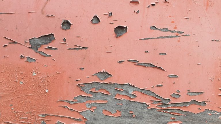 Close-up of a red wall with peeling paint revealing the surface beneath. Ideal for backgrounds.